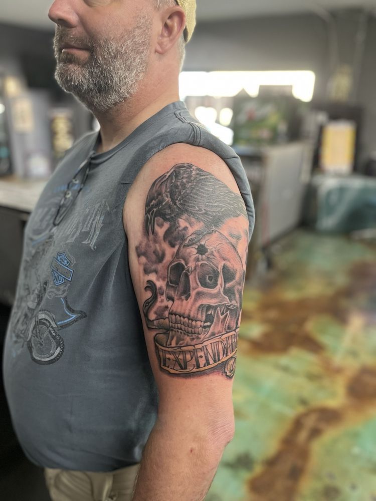 A man with a beard has a tattoo of a skull on his arm.