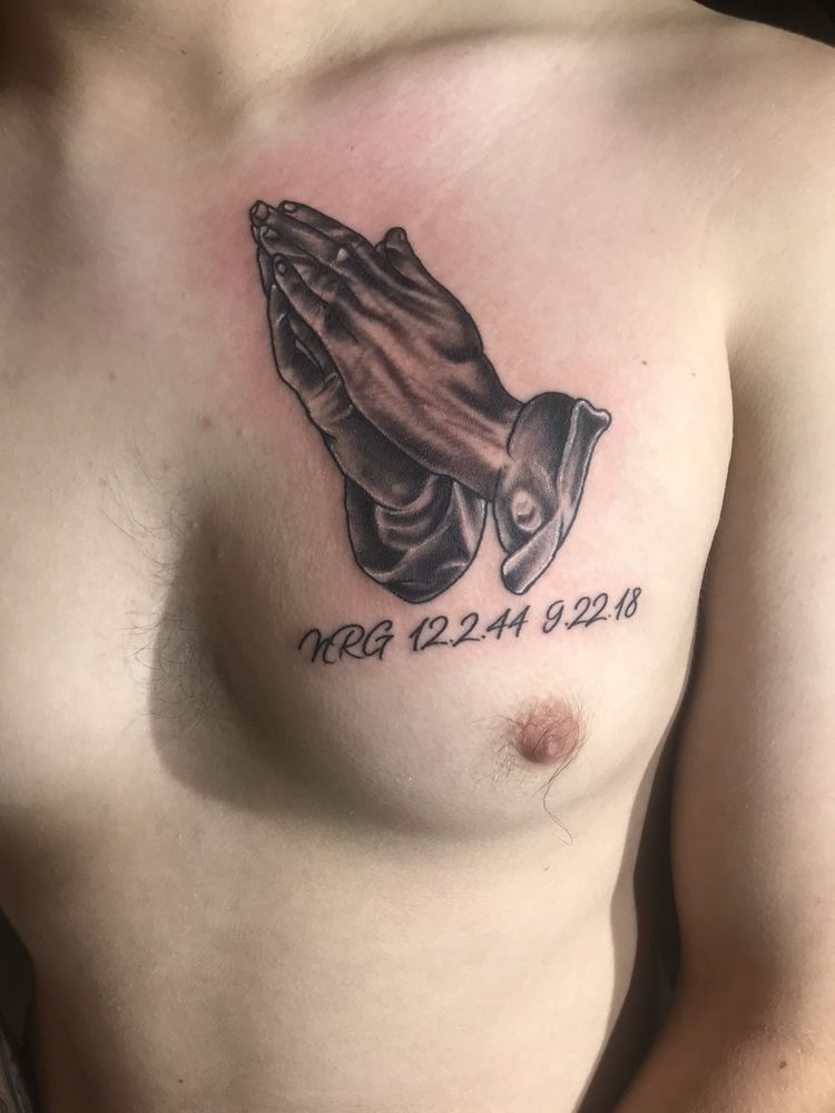 A man has a tattoo of praying hands on his chest.