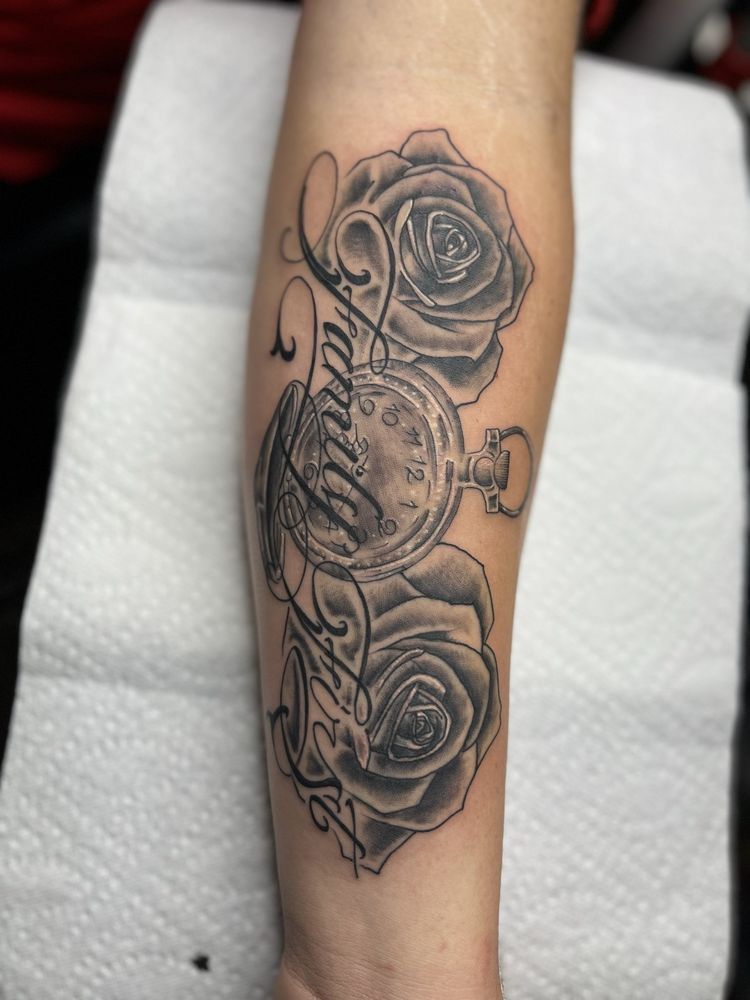 A person has a tattoo of roses and a pocket watch on their forearm.