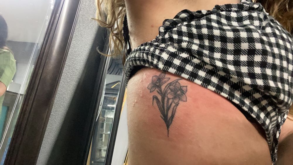 A woman has a tattoo of a flower on her shoulder.