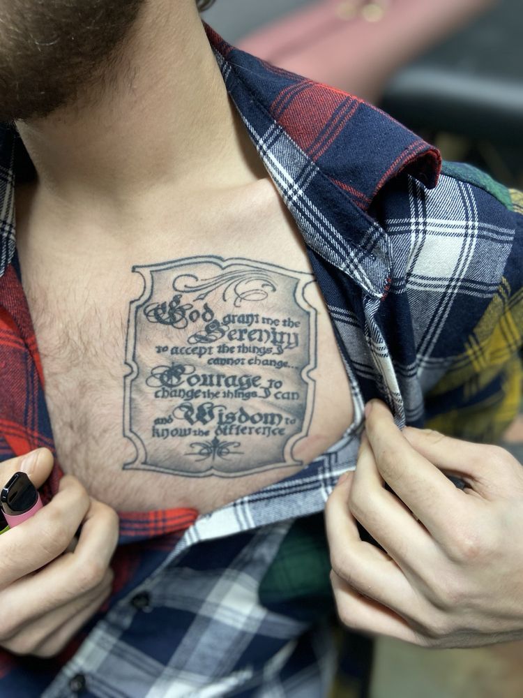A man in a plaid shirt has a tattoo on his chest