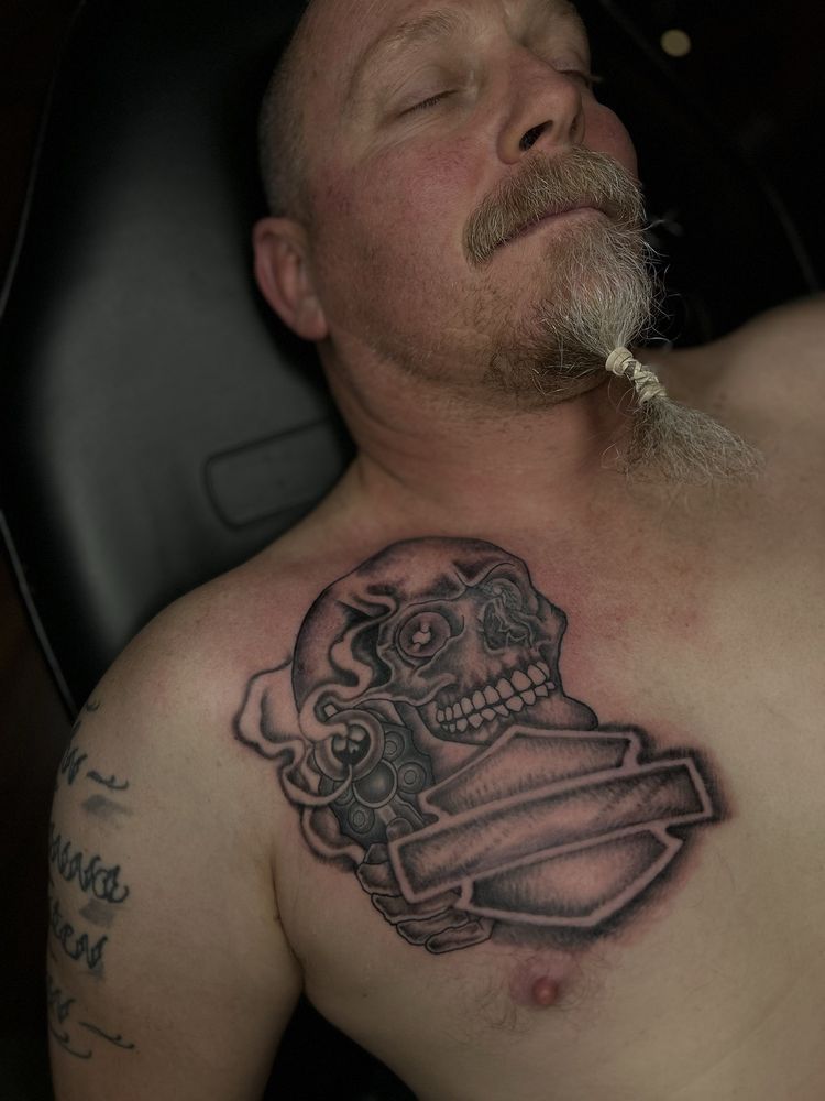A man with a beard has a tattoo of a skull on his chest.