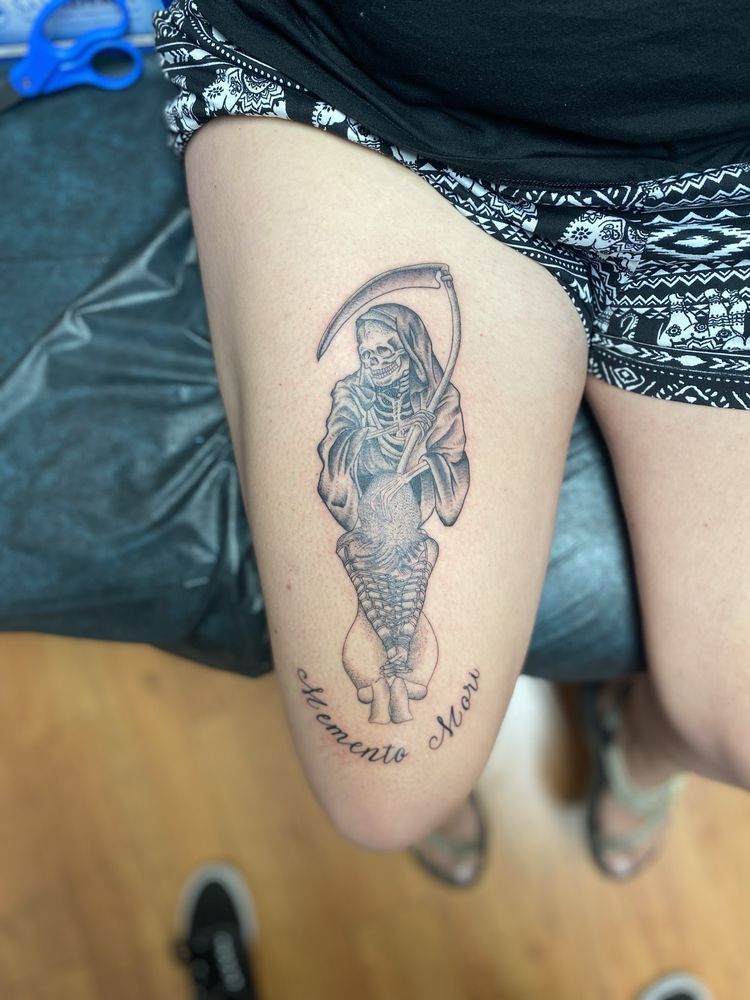 A woman has a tattoo of a grim reaper on her thigh.