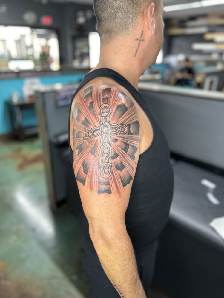 A man has a tattoo of a cross on his shoulder.