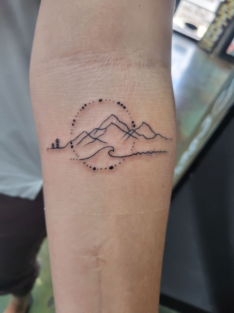 A person has a tattoo of a mountain and a wave on their forearm.