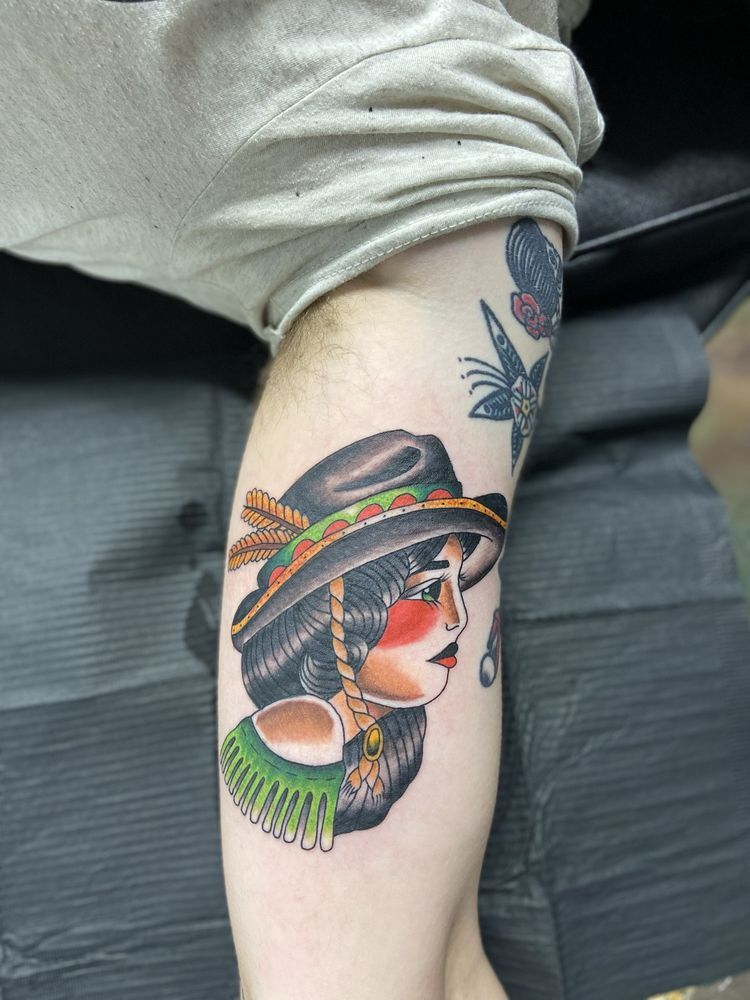 A person has a tattoo of a woman wearing a hat on their leg.