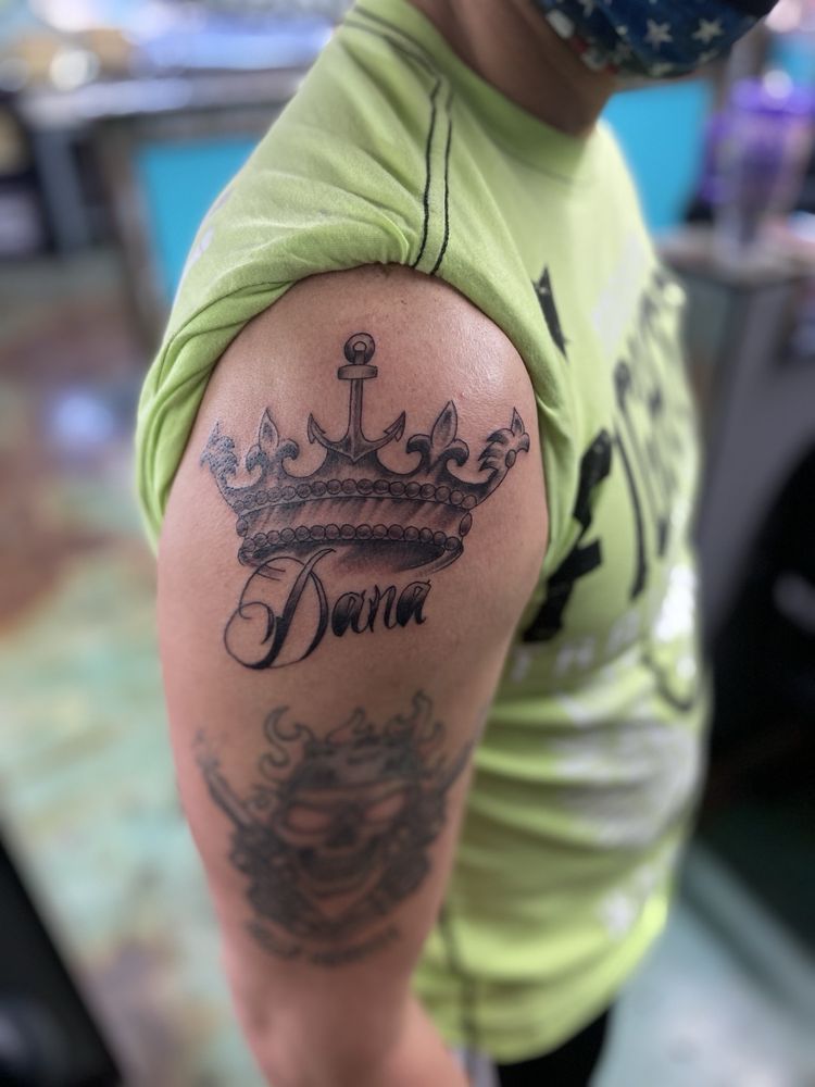 A woman has a tattoo of a crown and the name dana on her shoulder.