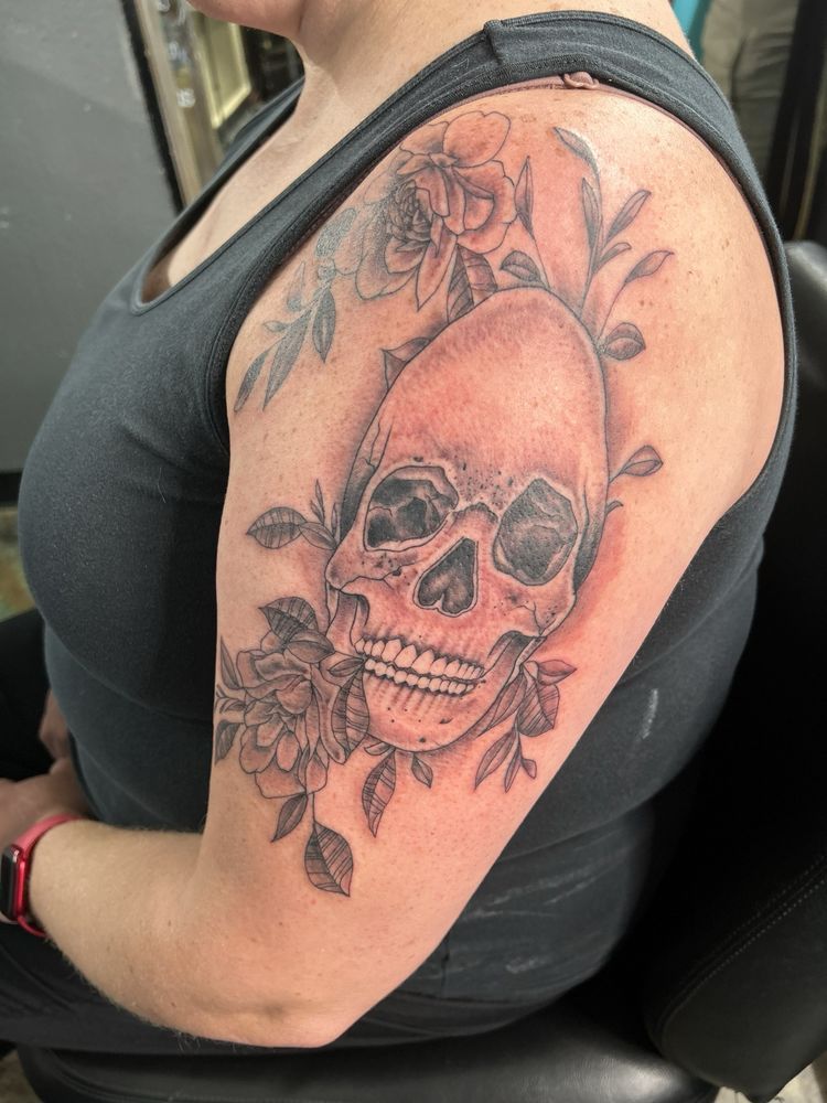 A woman has a tattoo of a skull and flowers on her arm.