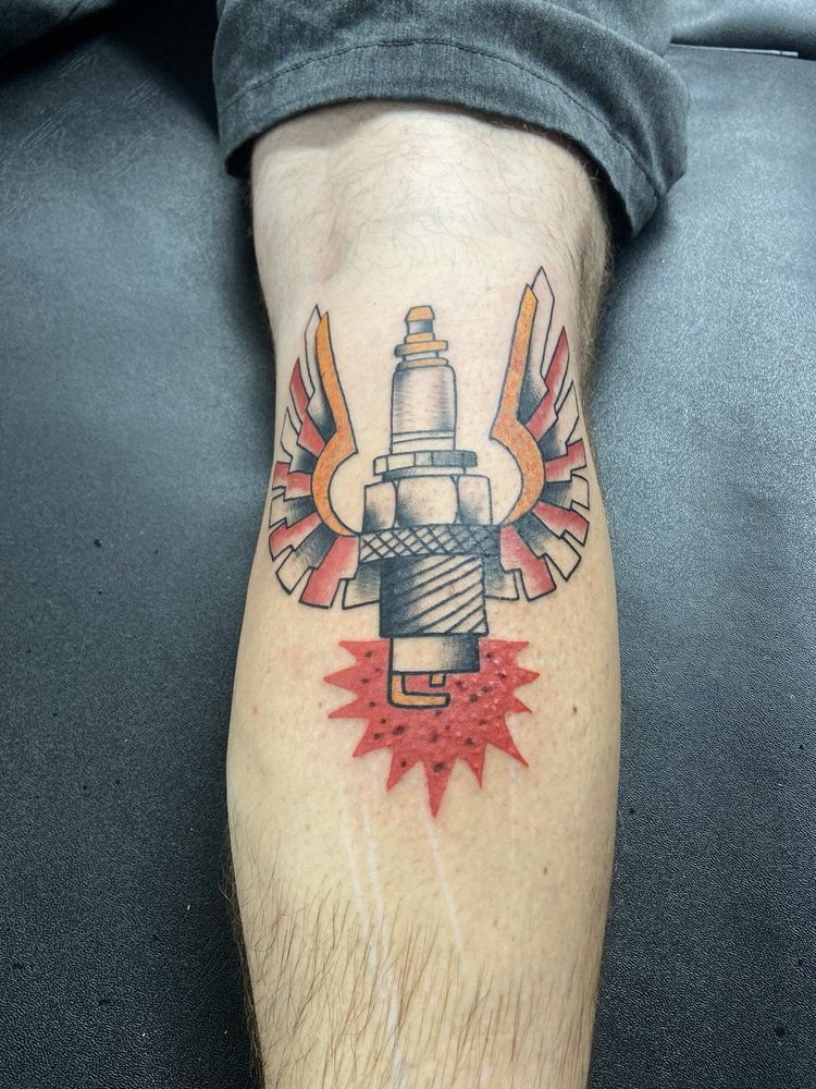A person has a tattoo of a spark plug with wings on their leg