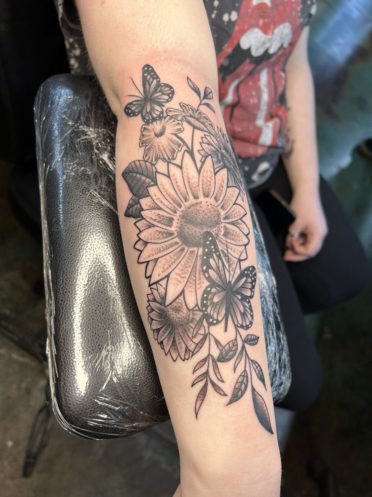 A woman has a tattoo of flowers and butterflies on her arm.