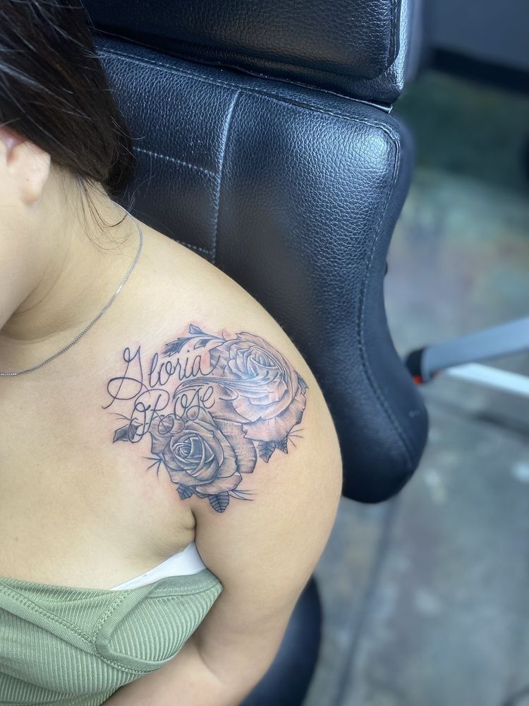 A woman has a tattoo of roses and the name gloria on her shoulder.