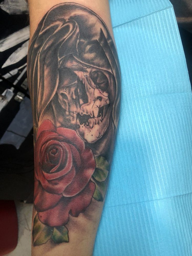 A tattoo of a grim reaper and a rose on a person 's arm.
