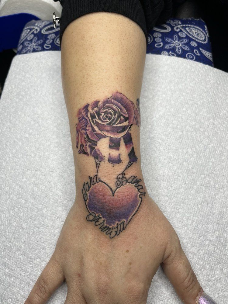 A woman has a tattoo of a heart and a rose on her wrist.