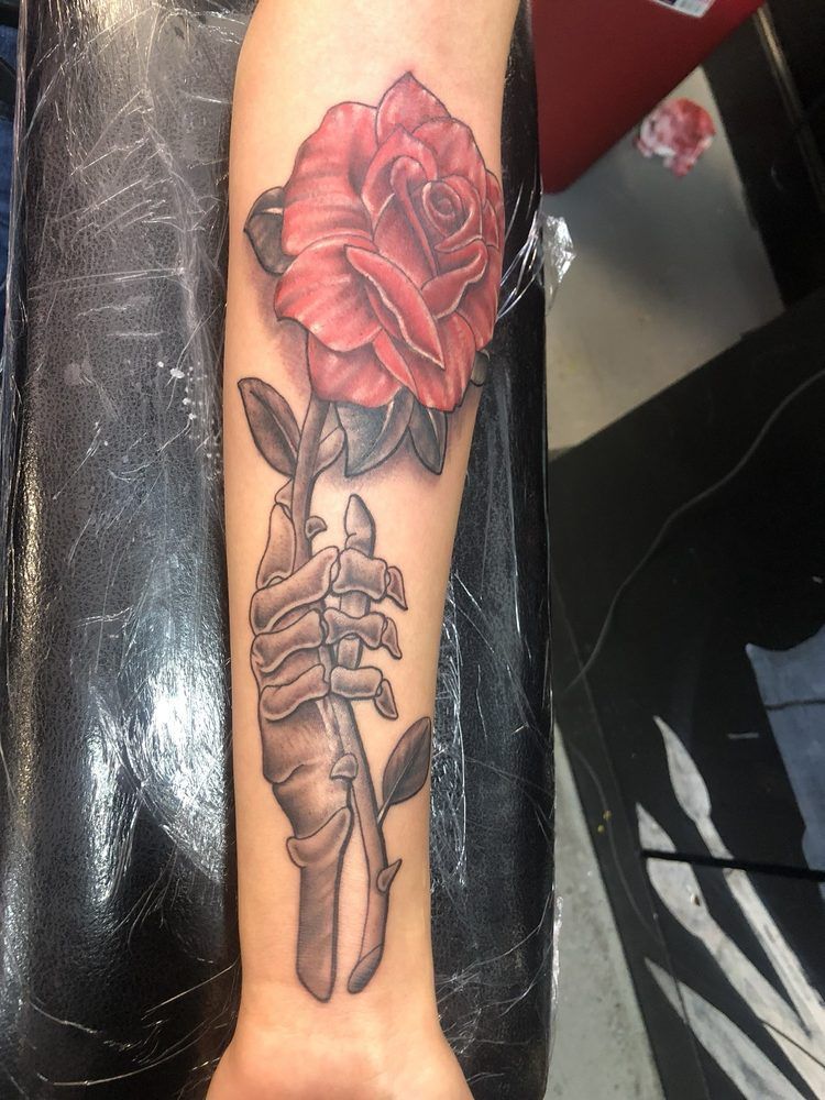 A tattoo of a skeleton hand holding a red rose