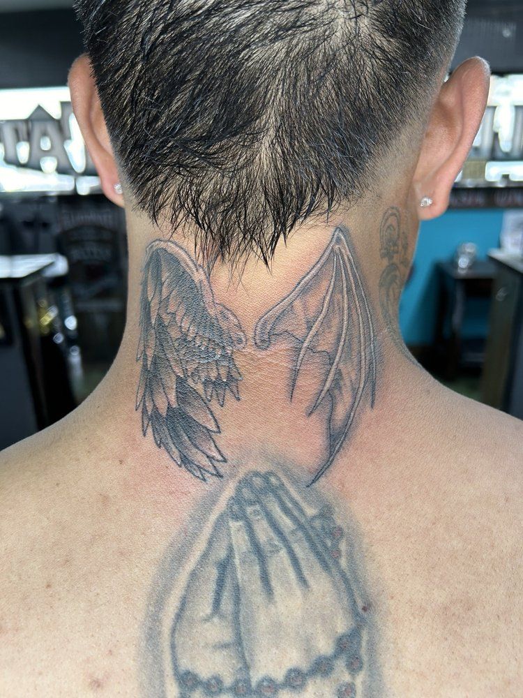 A man has a tattoo of praying hands and wings on his neck