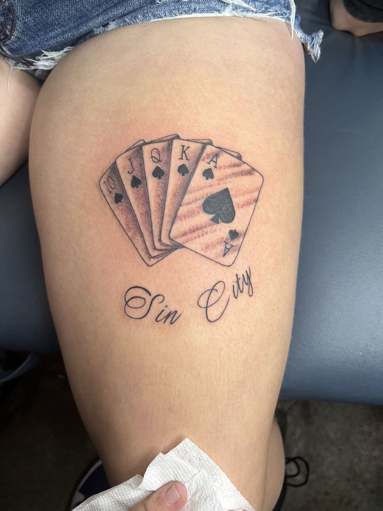 A woman has a tattoo of playing cards on her thigh.