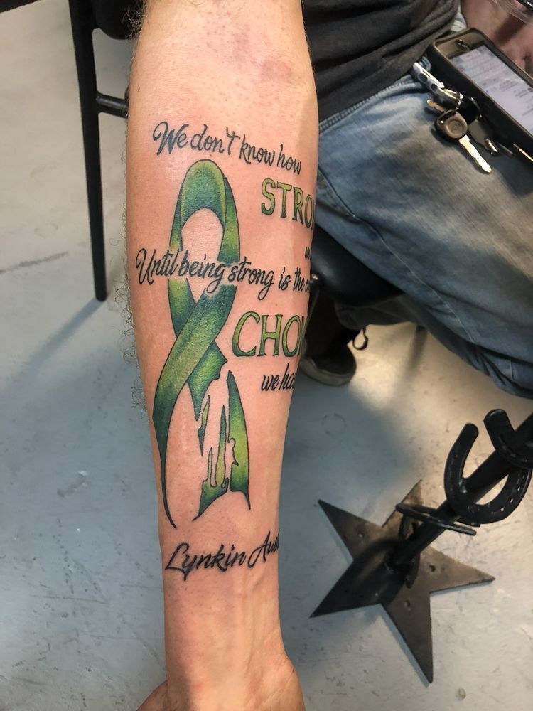 A man has a green ribbon tattoo on his leg