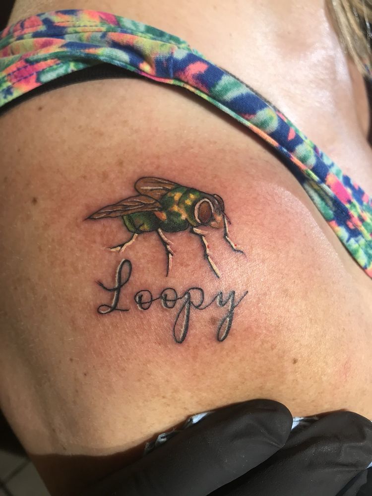 A woman has a tattoo of a fly and the word loopy on her back