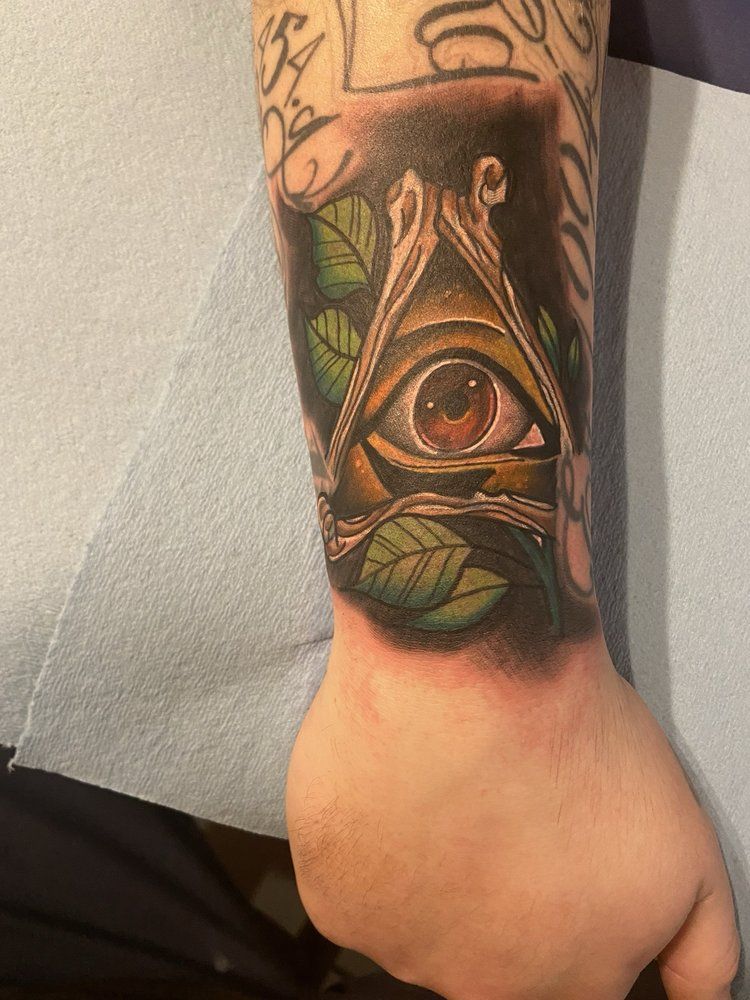 A man has a tattoo of an all seeing eye on his wrist.