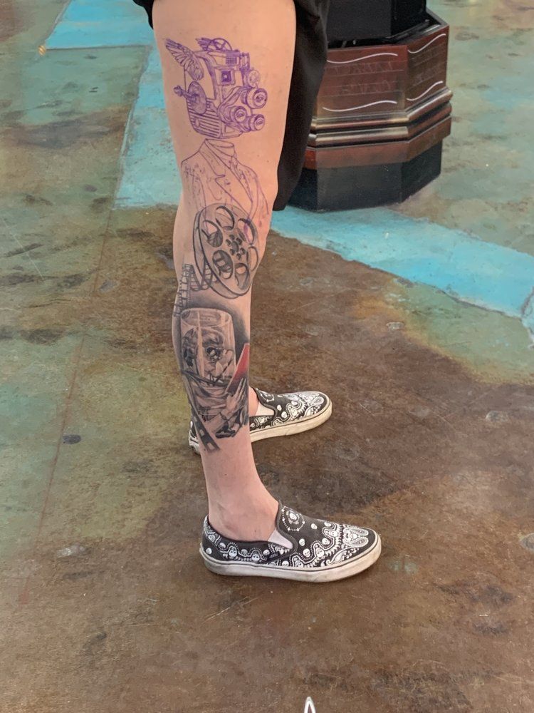 A person with a tattoo on their leg is wearing a pair of shoes.