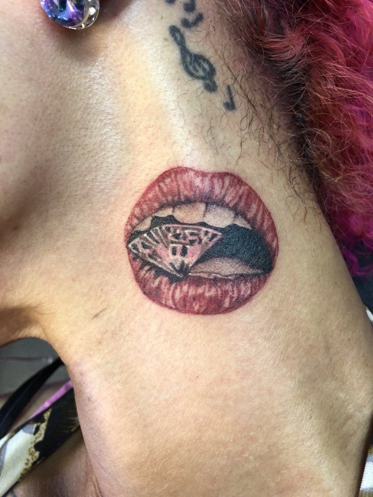 A woman has a tattoo of a woman 's mouth with a diamond in it.