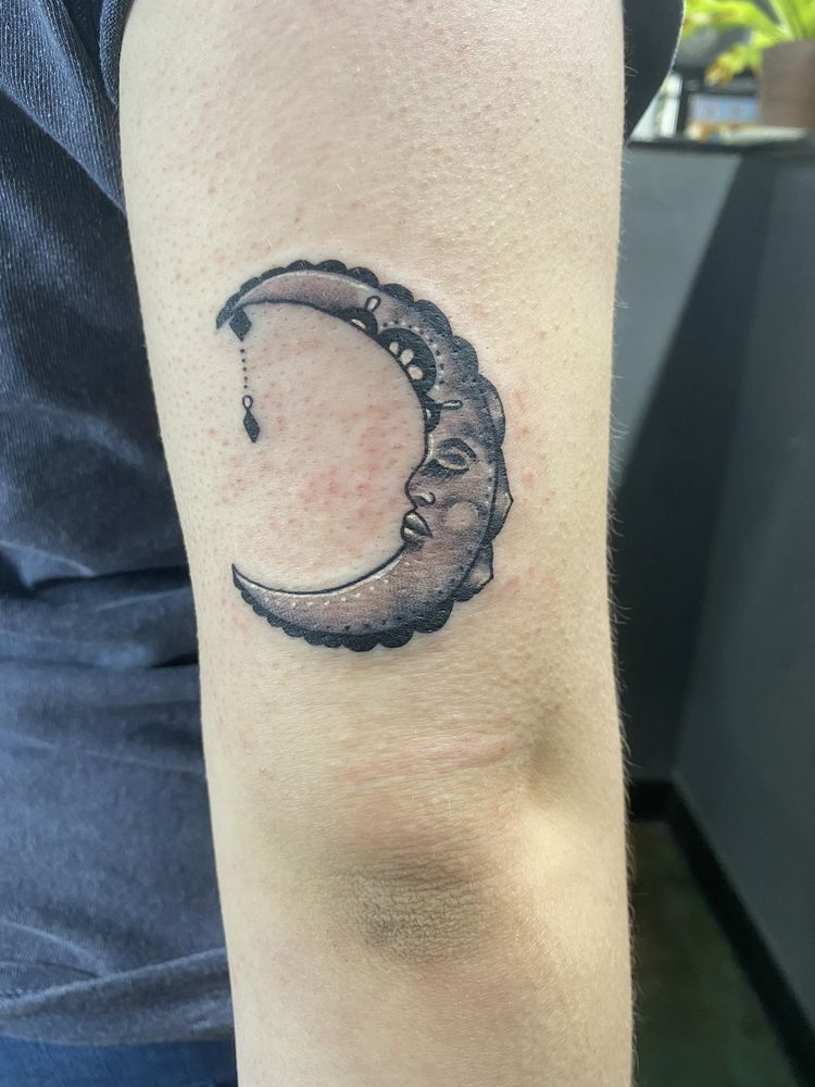 A tattoo of a crescent moon with a face on it