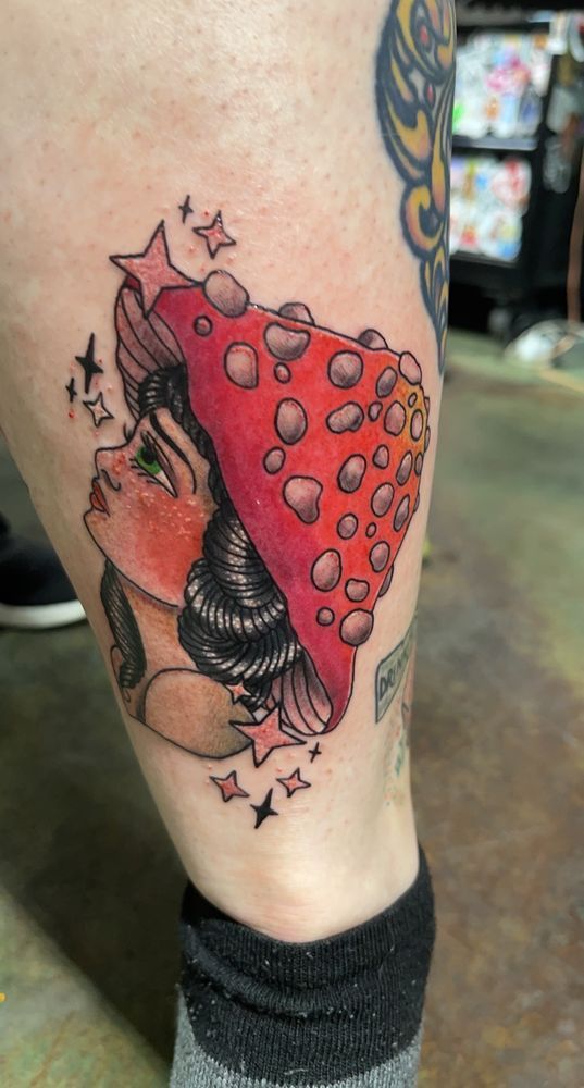 A tattoo of a woman wearing a red mushroom hat on her leg.