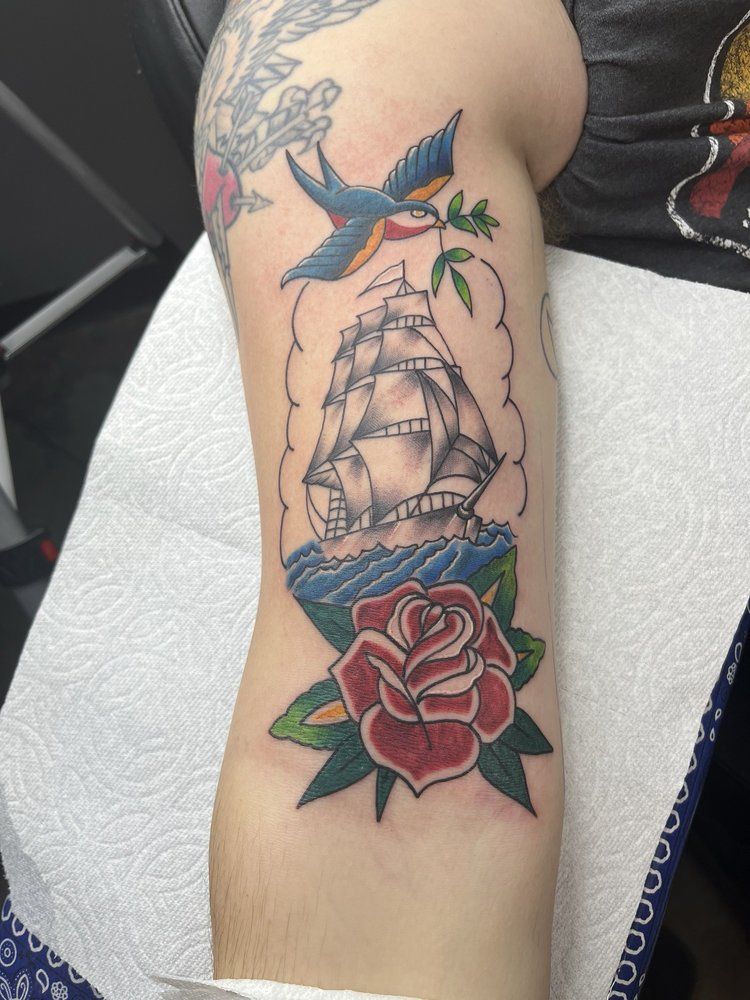 A tattoo of a ship and a rose on a person 's arm