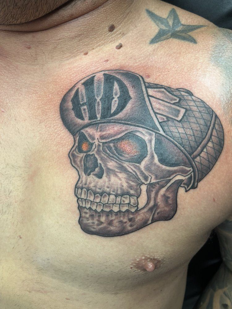 A man has a tattoo of a skull wearing a hat on his chest.