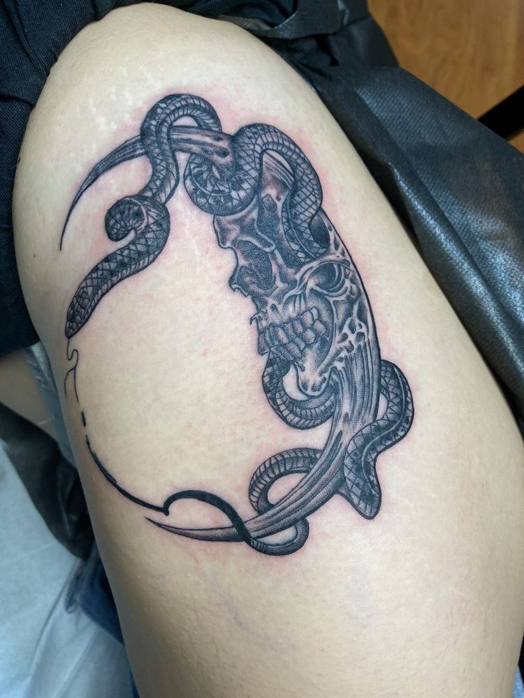 A person has a tattoo of a skull and snakes on their thigh
