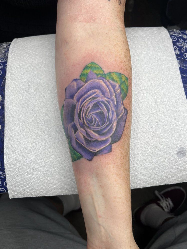 A person has a tattoo of a purple rose on their forearm.
