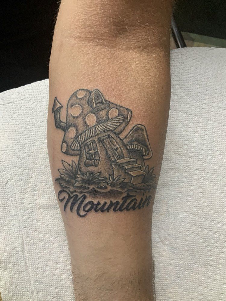 A person has a tattoo of a mushroom house on their forearm.