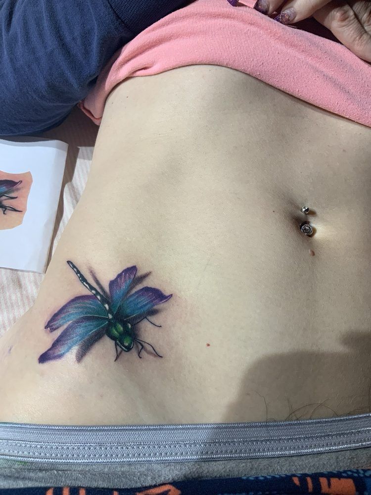 A woman has a dragonfly tattoo on her stomach