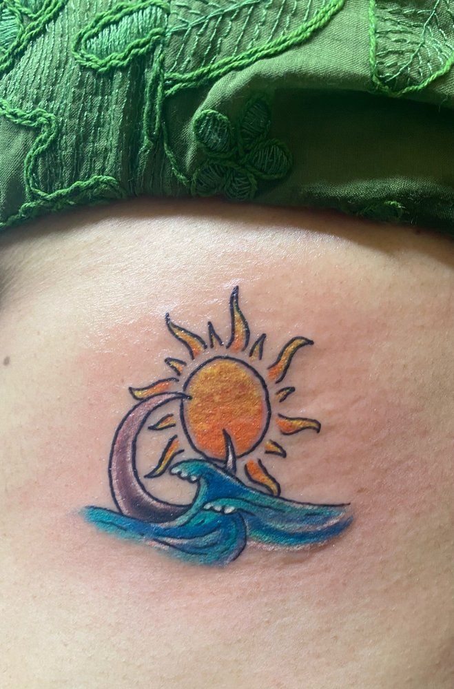 A person has a tattoo of a sun and waves on their side.