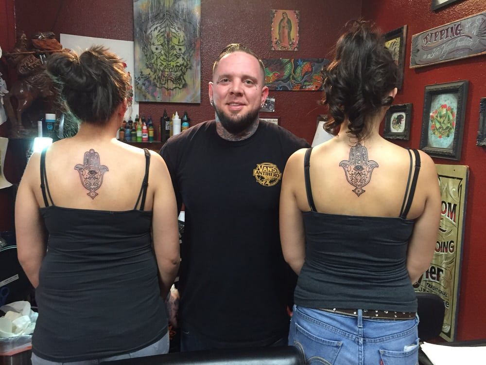 A man is standing between two women with tattoos on their backs.