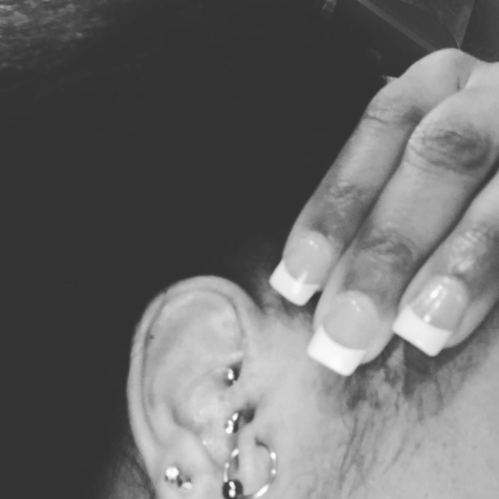 A black and white photo of a woman 's ear with piercings and french manicure.