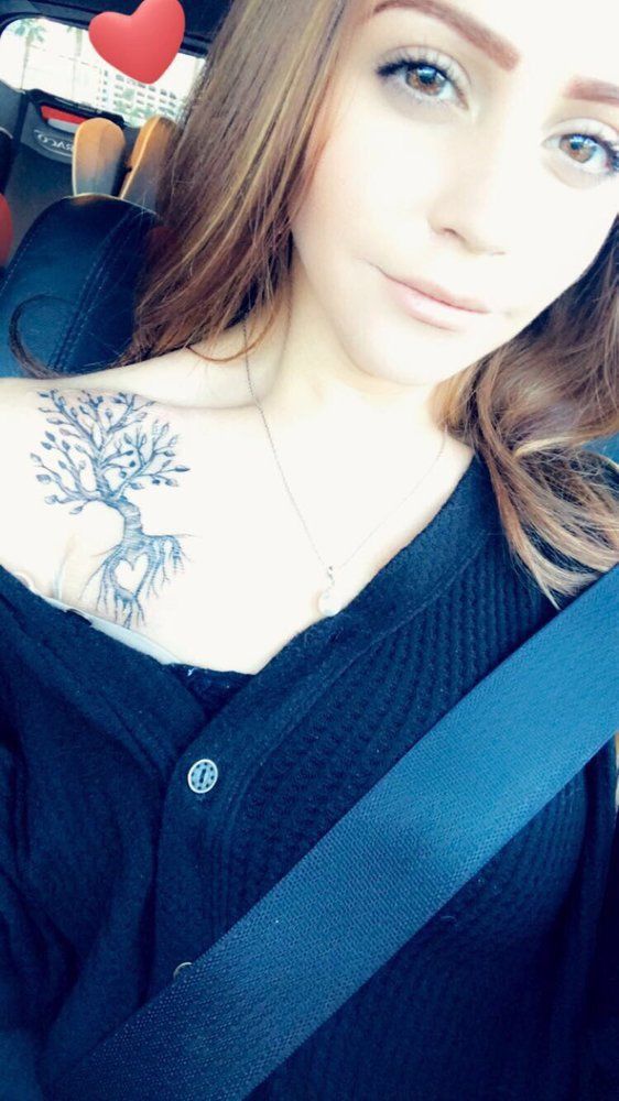 A woman with a tree tattoo on her shoulder is taking a selfie in a car.