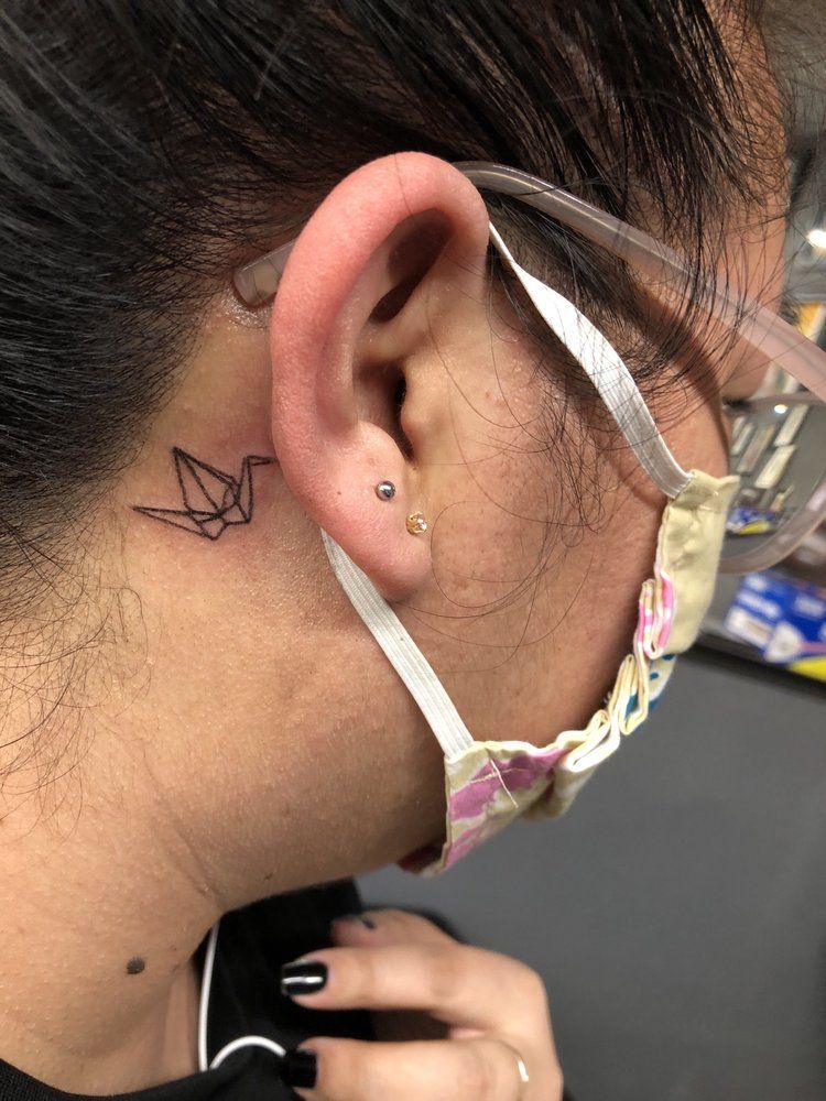A woman with a tattoo of an origami crane behind her ear.
