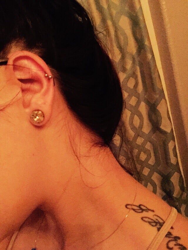 A close up of a woman 's ear with earrings and a tattoo on her shoulder