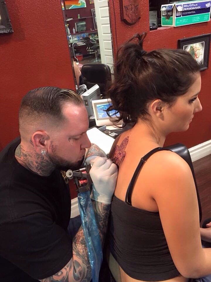 A woman is getting a tattoo on her back by a tattoo artist.