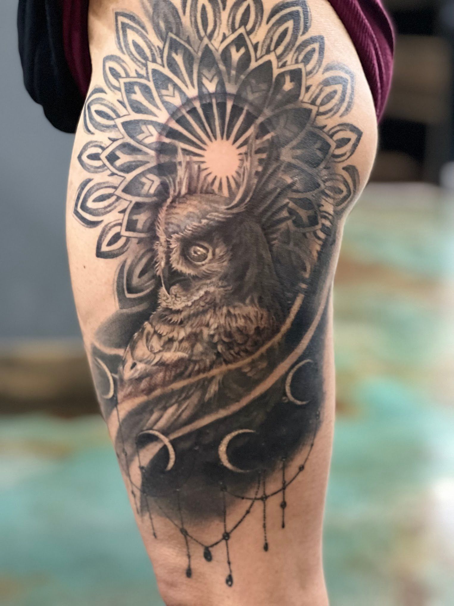 A person has a tattoo of an owl and a mandala on their thigh.