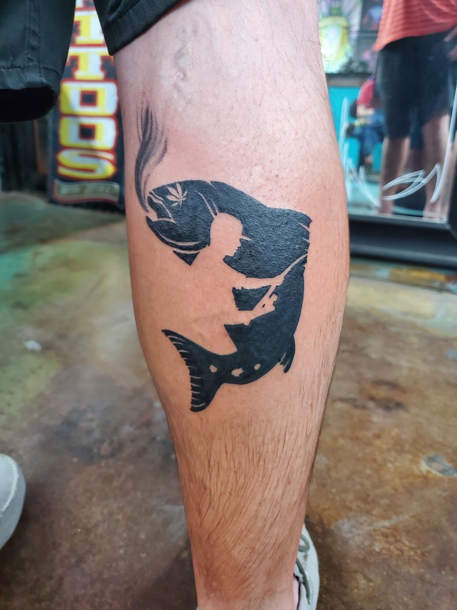 A man has a tattoo of a fish on his leg.