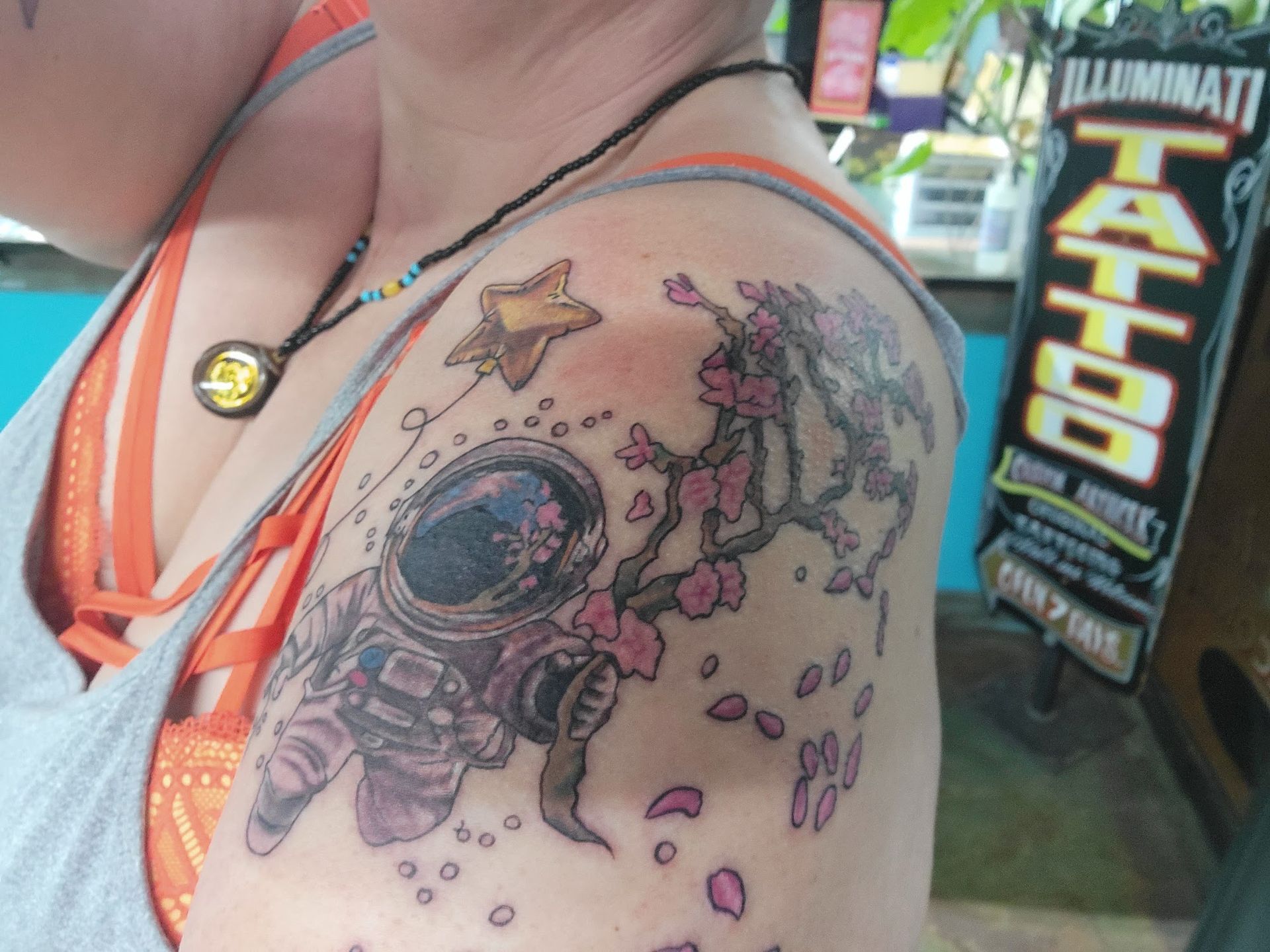 A woman has a tattoo of an astronaut and flowers on her shoulder