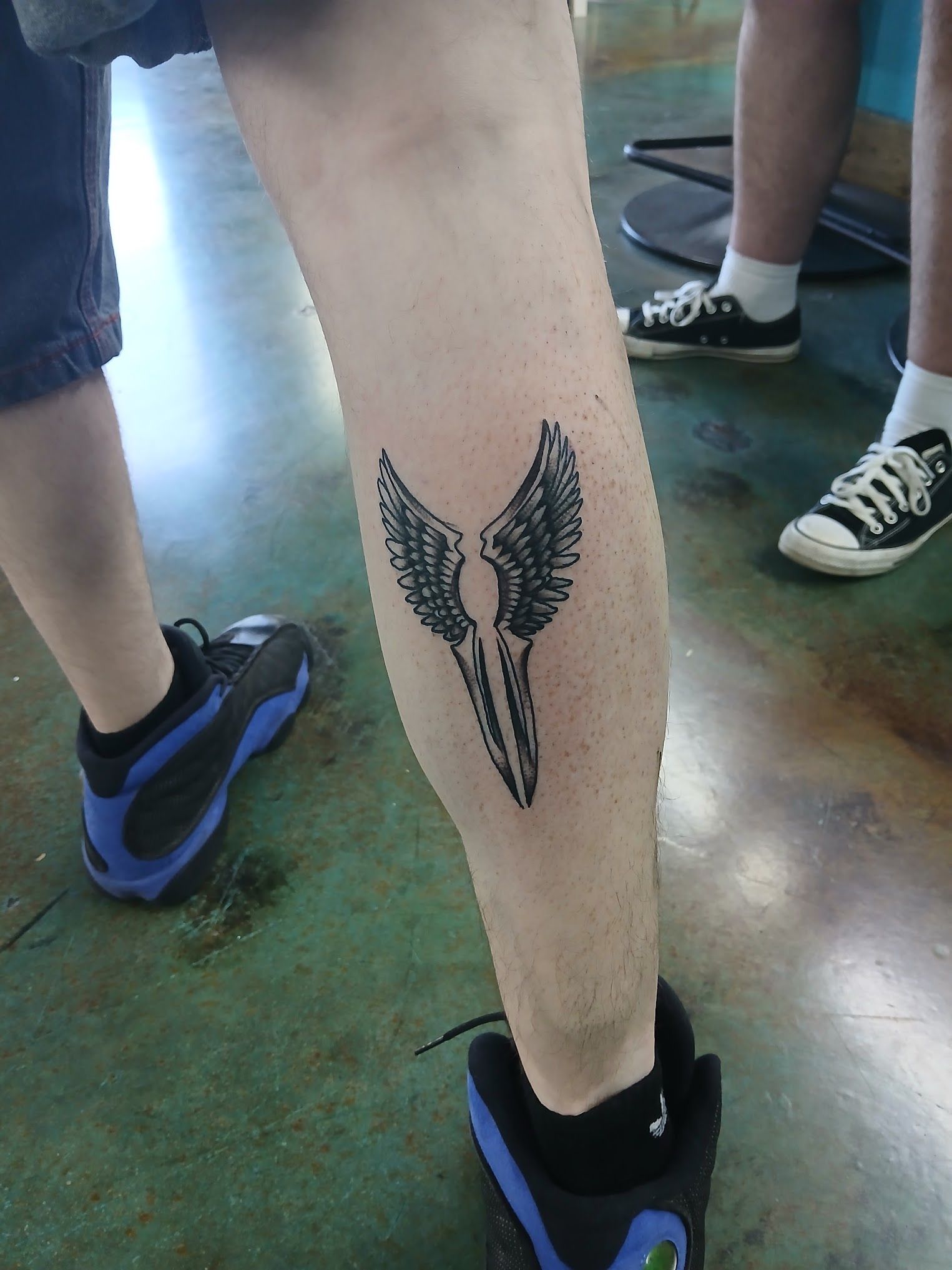 A person has a tattoo of a skull with wings on their leg