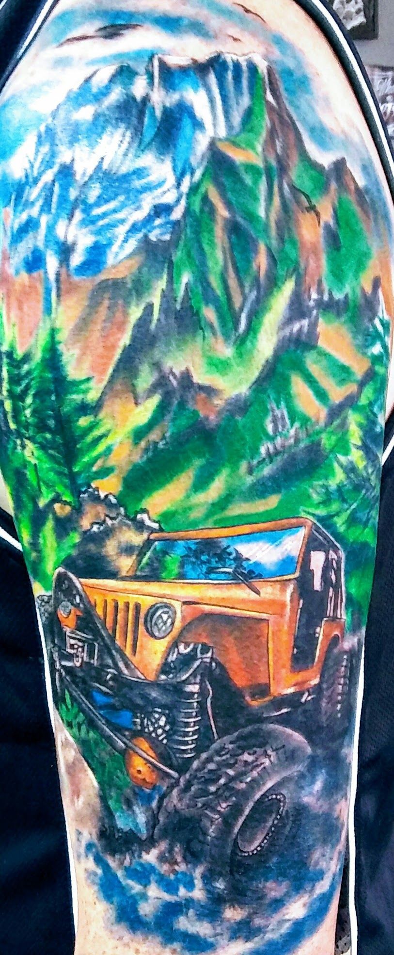A person has a tattoo of a jeep and mountains on their arm.