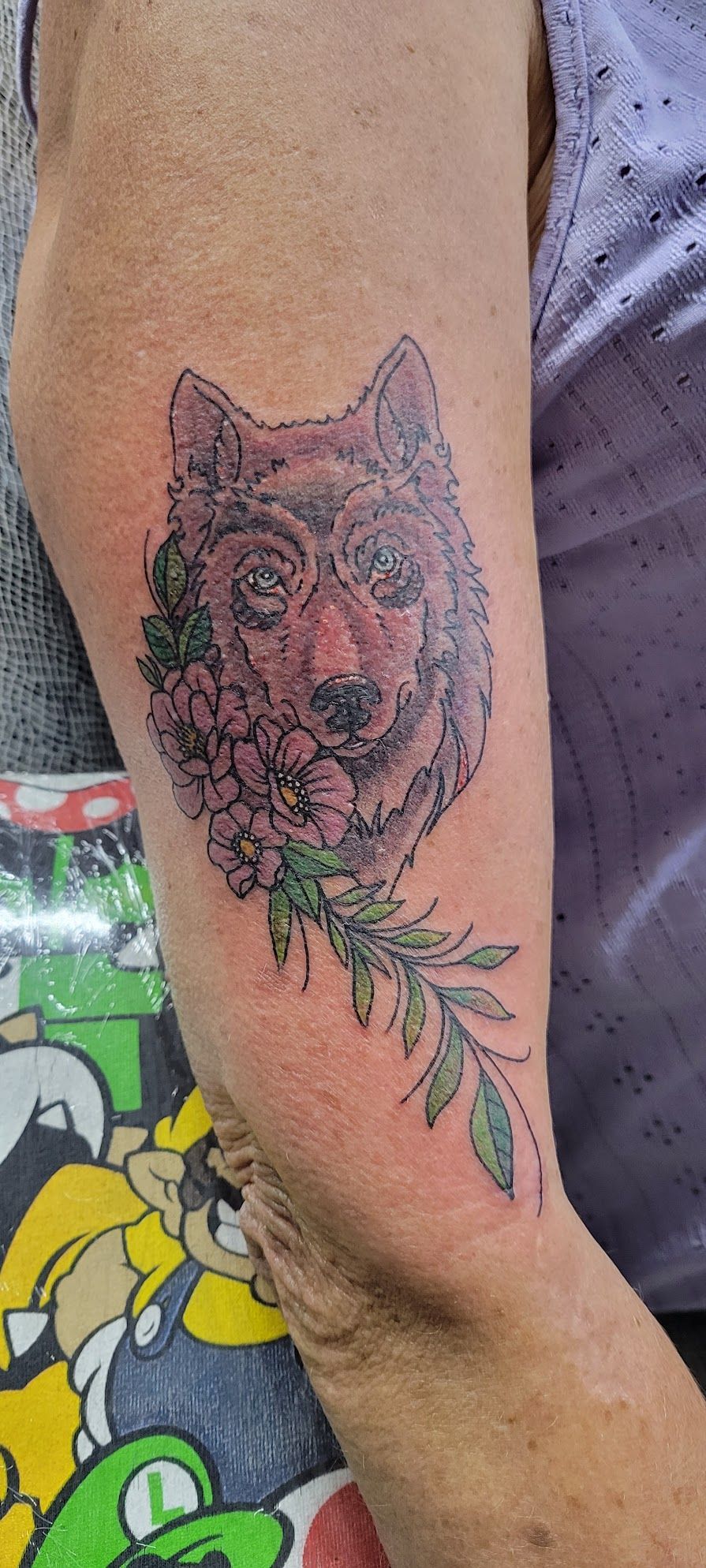 A woman has a tattoo of a wolf with flowers on her arm.