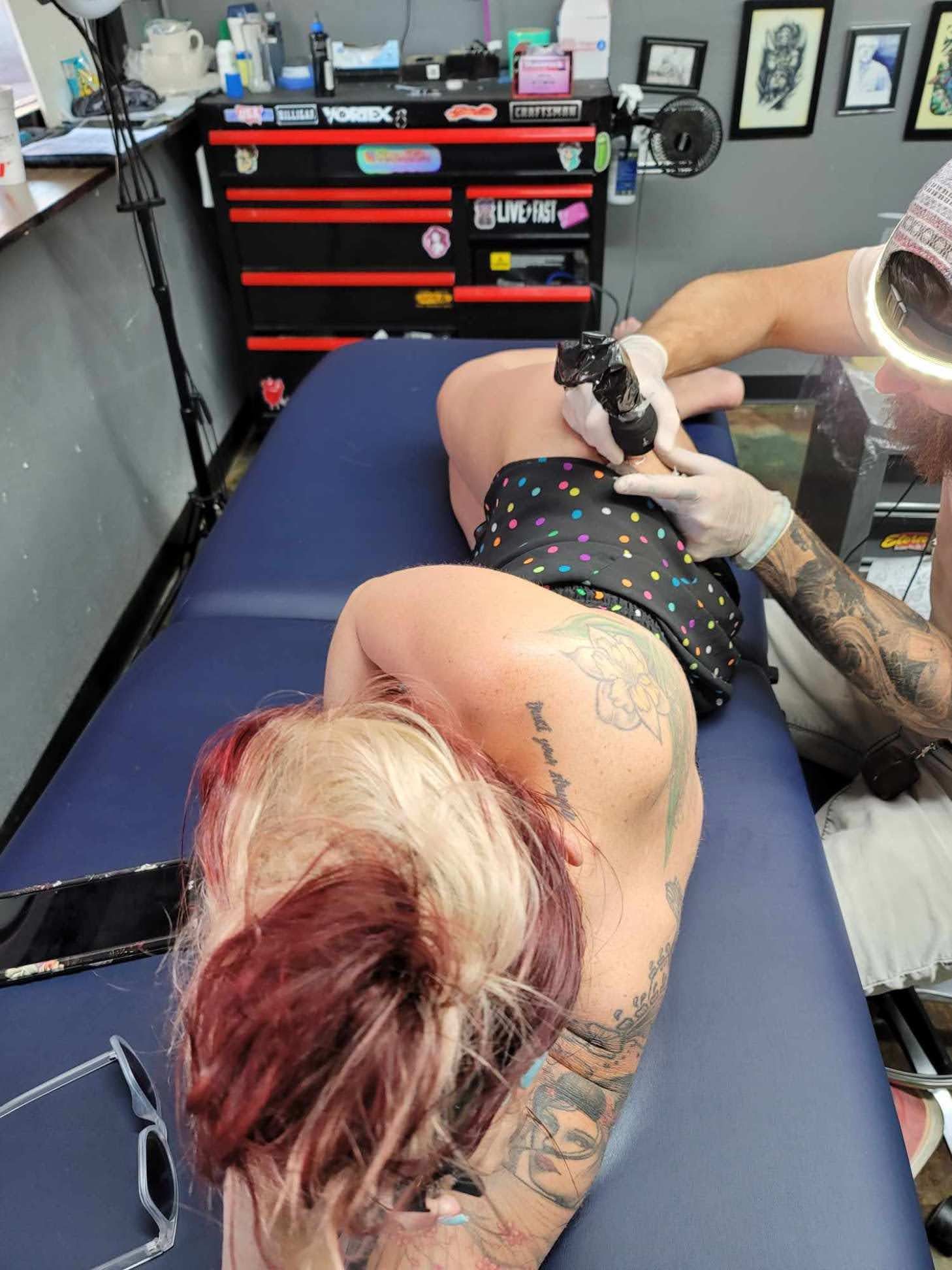 A woman is laying on a bed getting a tattoo on her back.