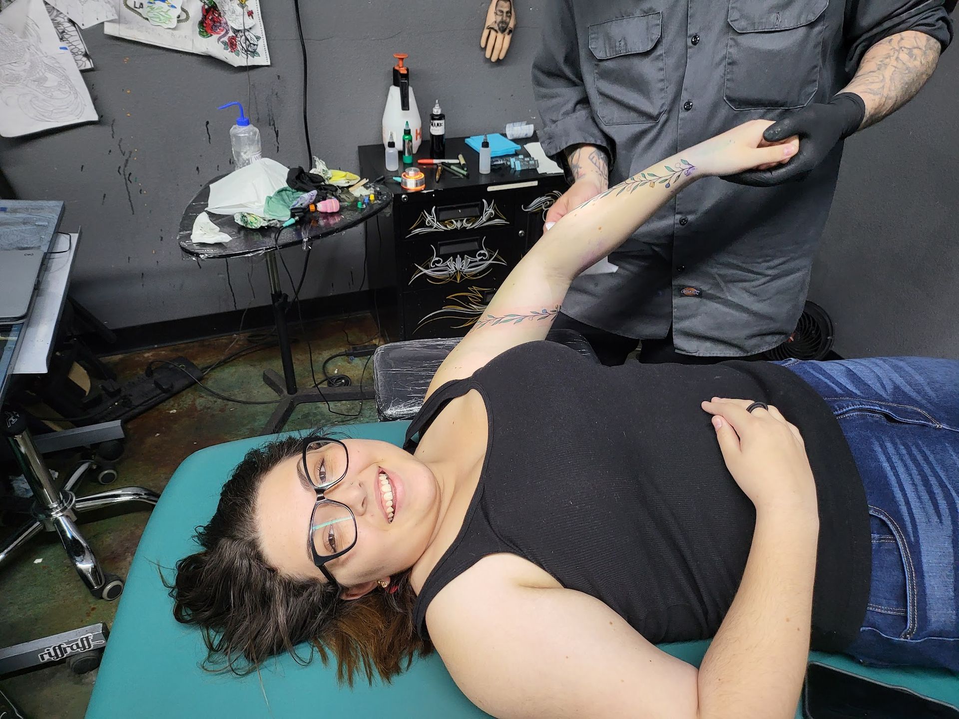 A woman is laying on a table getting a tattoo on her arm.