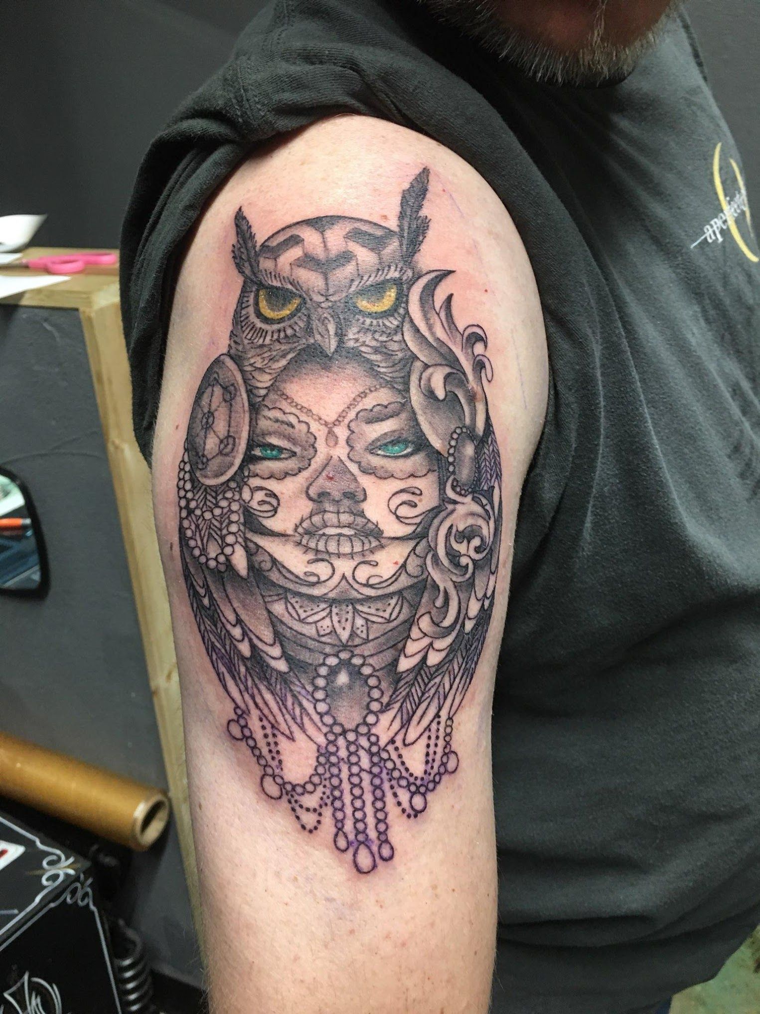 A man has a tattoo of an owl and a woman 's face on his arm.