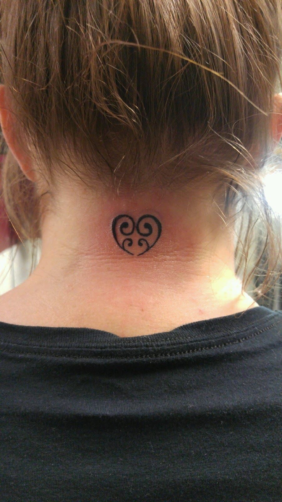 A woman has a small heart tattoo on the back of her neck.